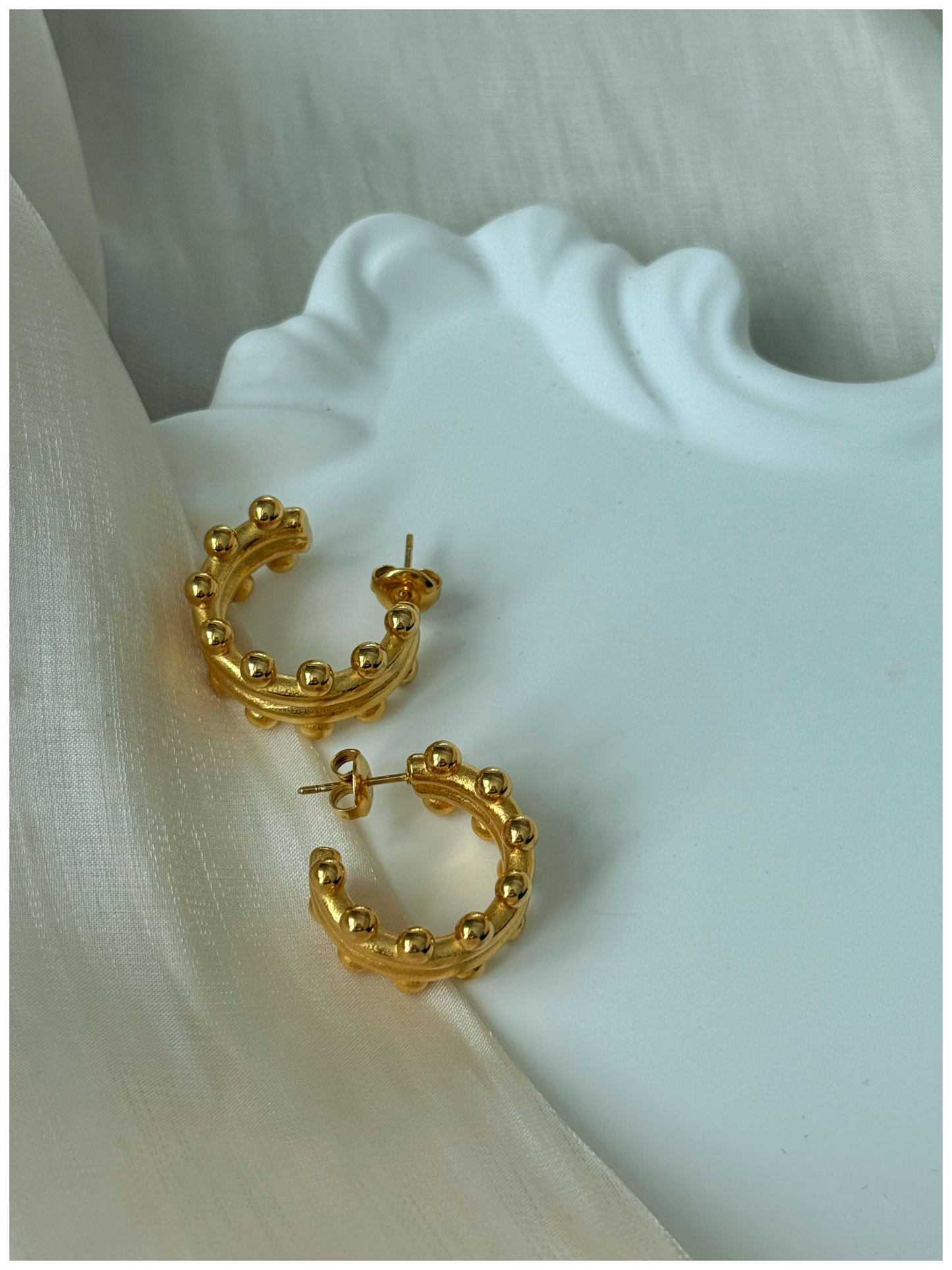 Gold hoop earrings on a white fabric background