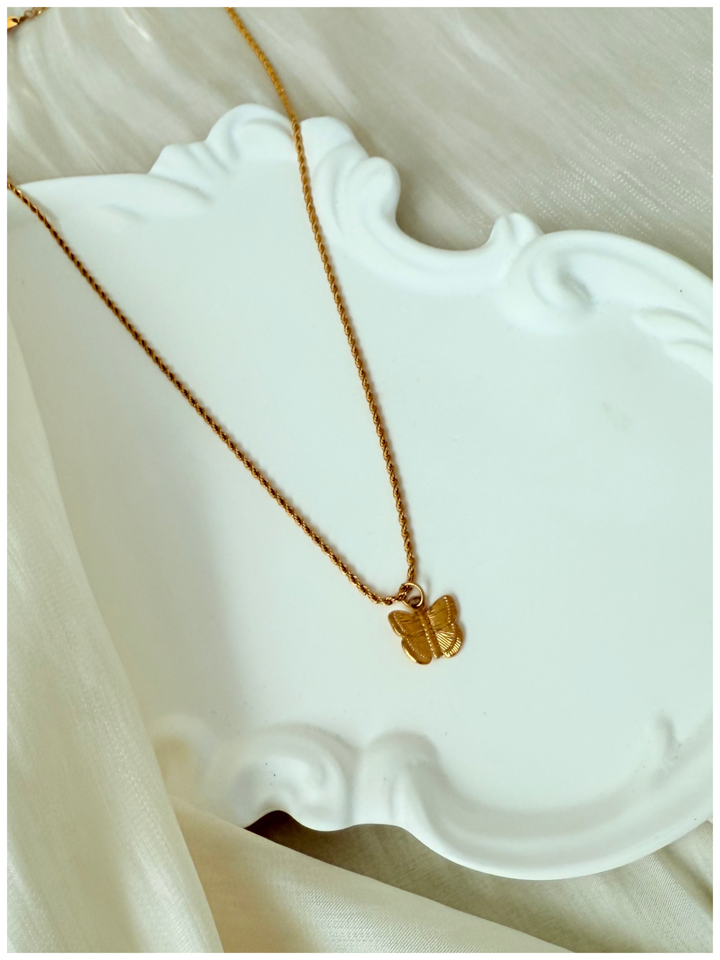 Gold necklace with a butterfly pendant on a white dish