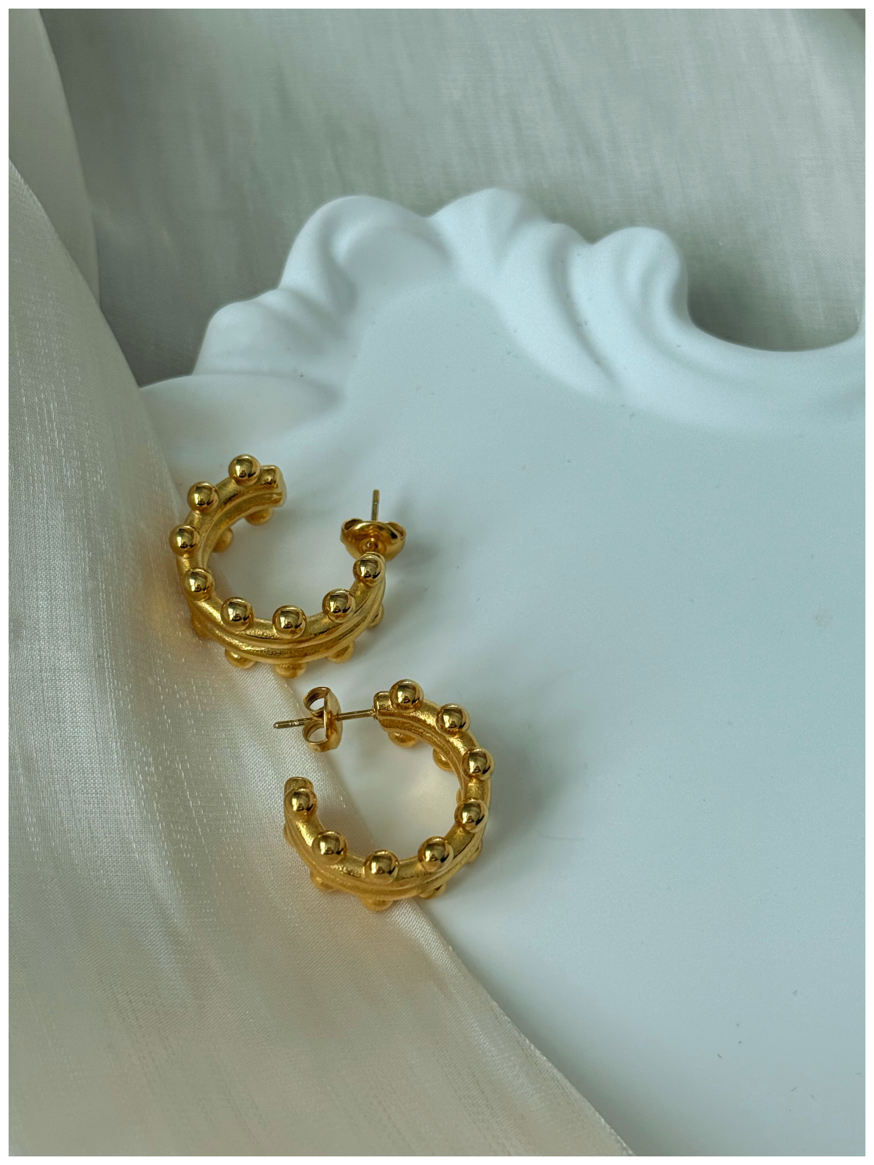 Gold hoop earrings on a white fabric background